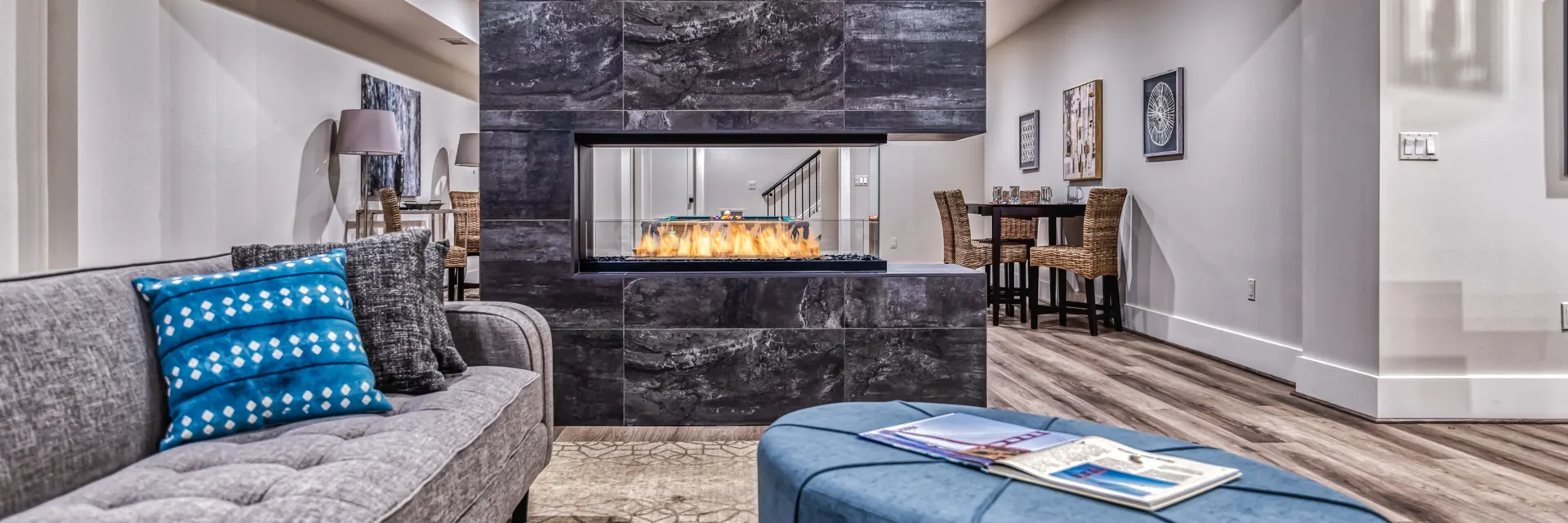 EcoSmart Fire Flex peninsula fireplace burning in a dark stone surround in a living room with a gray sofa and a blue ottoman