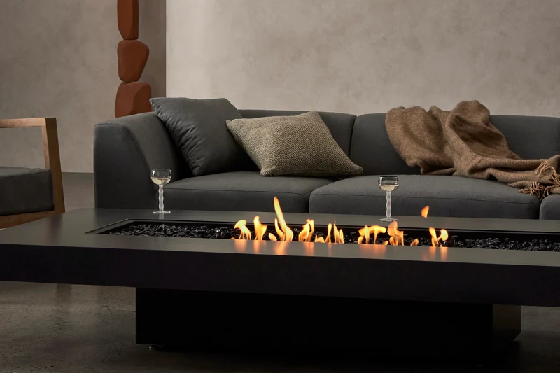 EcoSmart Gin 90 Low fire table in black with a line of flame in front of a dark sofa and a plaster wall