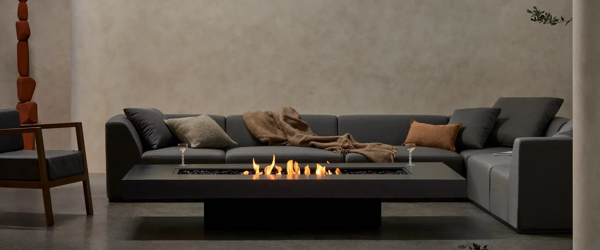 Black EcoSmart Gin 90 Low bioethanol fire table with a line of flames in front of a dark grey corner sofa, against a plain plastered wall