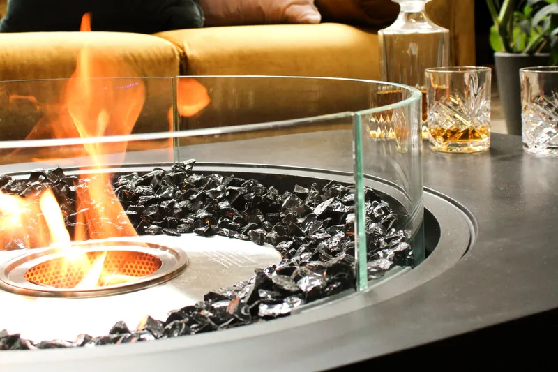 Close view of an EcoSmart Martini 50 bioethanol fire table burning behind a round glass screen, with a mustard sofa behind