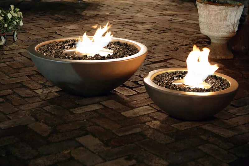 Two EcoSmart Mix fire bowls burning on a brick-paved courtyard at night, with potted plants behind