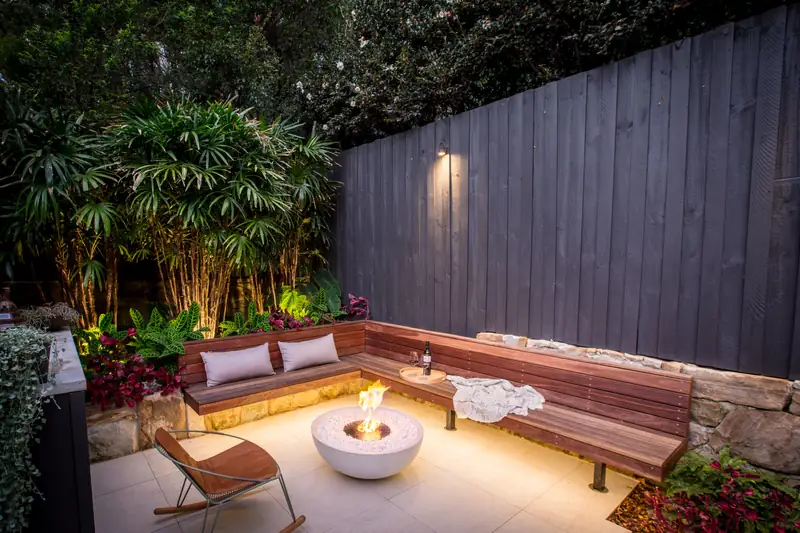 EcoSmart Mix 850 fire bowl burning in a courtyard at night, with a lit timber bench, bamboo and a dark fence