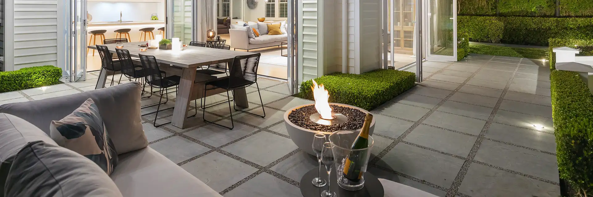 EcoSmart Mix 850 fire bowl burning on the paved patio of a white weatherboard house, beside an outdoor dining table at dusk