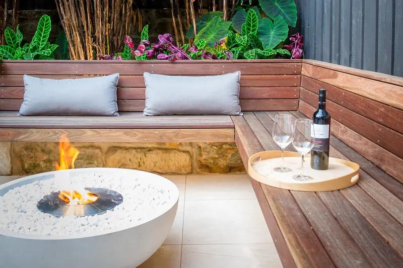 EcoSmart Mix 850 fire bowl in white burning beside a timber bench with cushions and tropical plants