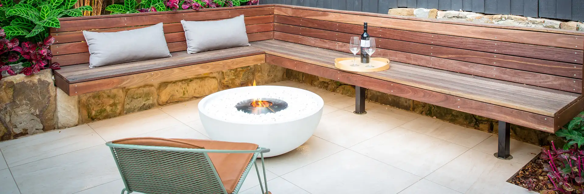EcoSmart Mix 850 fire bowl in white in a paved courtyard beside a long timber corner bench with cushions