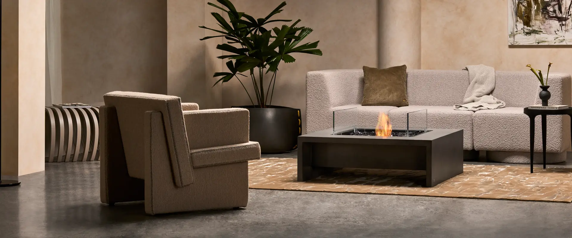 Square EcoSmart Mojito 40 fire table burning between a sculptural armchair and a pale sofa in a lounge with plaster walls
