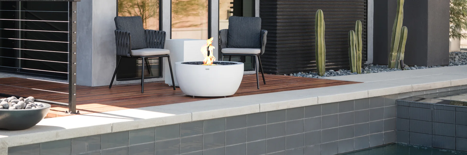 EcoSmart Pod 30 fire pit in white on the timber deck of a dark modern house, with two chairs beside a pool