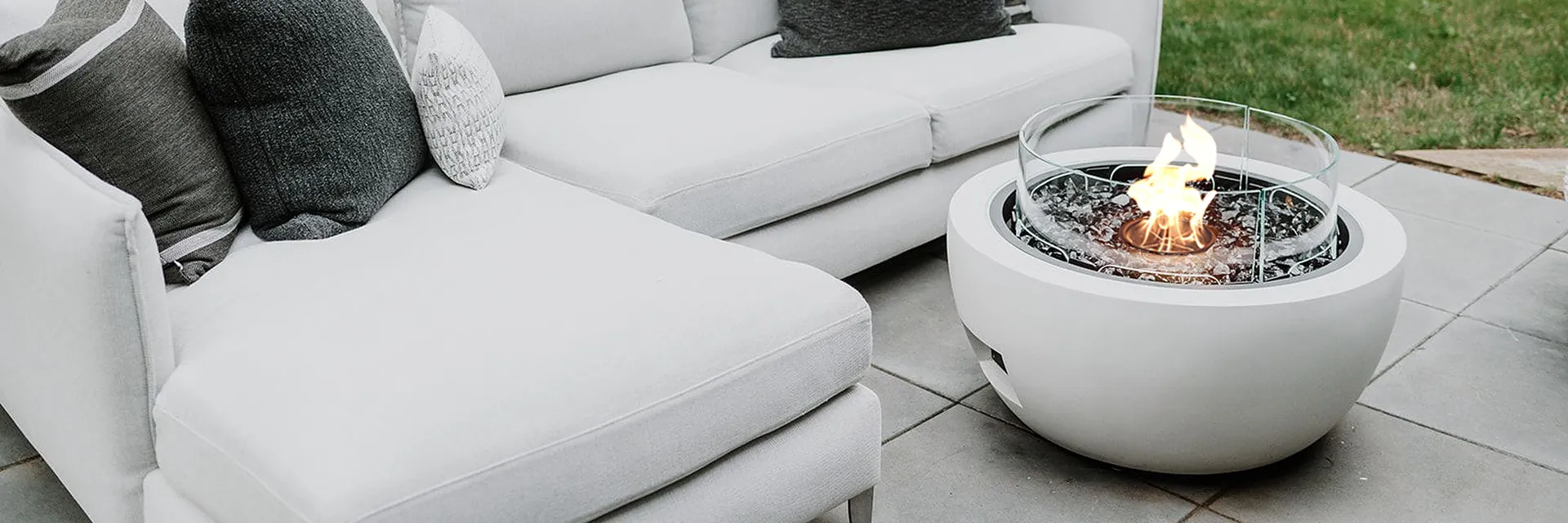 EcoSmart Pod 30 fire pit in white burning beside a white corner sofa with gray cushions on a garden lawn
