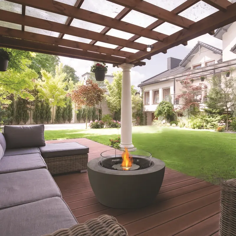 Dark EcoSmart Pod 40 bioethanol fire bowl with a glass screen on a timber deck under a pergola, beside an outdoor sofa and facing a lawn and houses