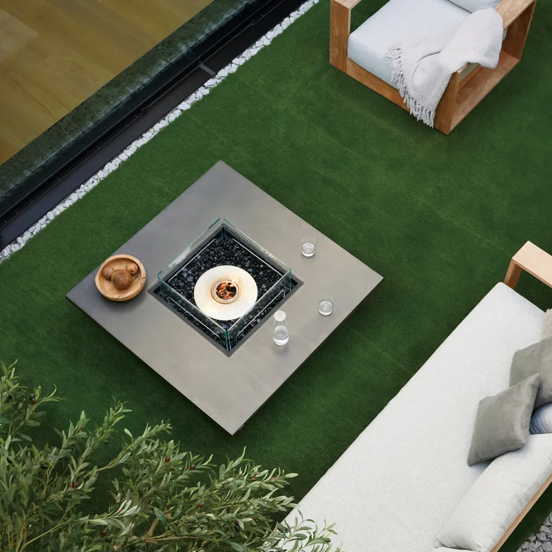 Square EcoSmart Vertigo fire table seen from above on a lawn, beside a pale sofa and a teak armchair