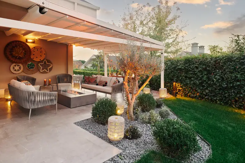 EcoSmart Wharf 65 fire table burning in the porch of a house at dusk, beside a tree, a lawn and garden lights