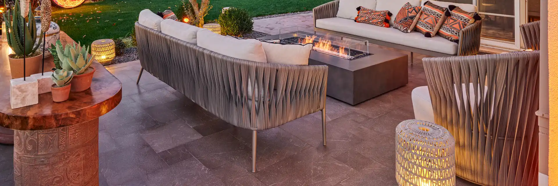 EcoSmart Wharf 65 fire table burning in front of rope sofas on the covered terrace of a house, with a garden behind