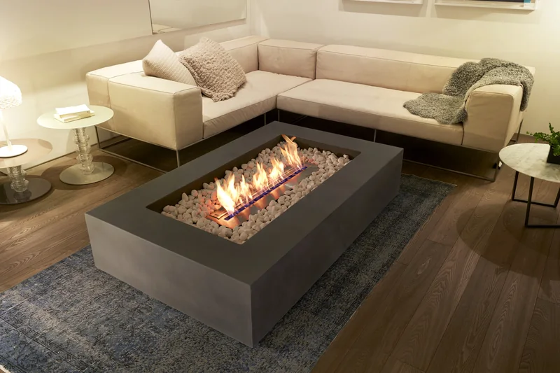 Large rectangular concrete EcoSmart Wharf 65 bioethanol fire table with flames over pale stones, in a living room with a cream corner sofa and a timber floor