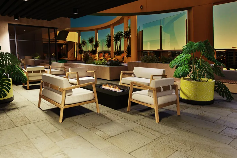 EcoSmart Wharf 65 fire table burning between teak armchairs on a paved terrace at dusk