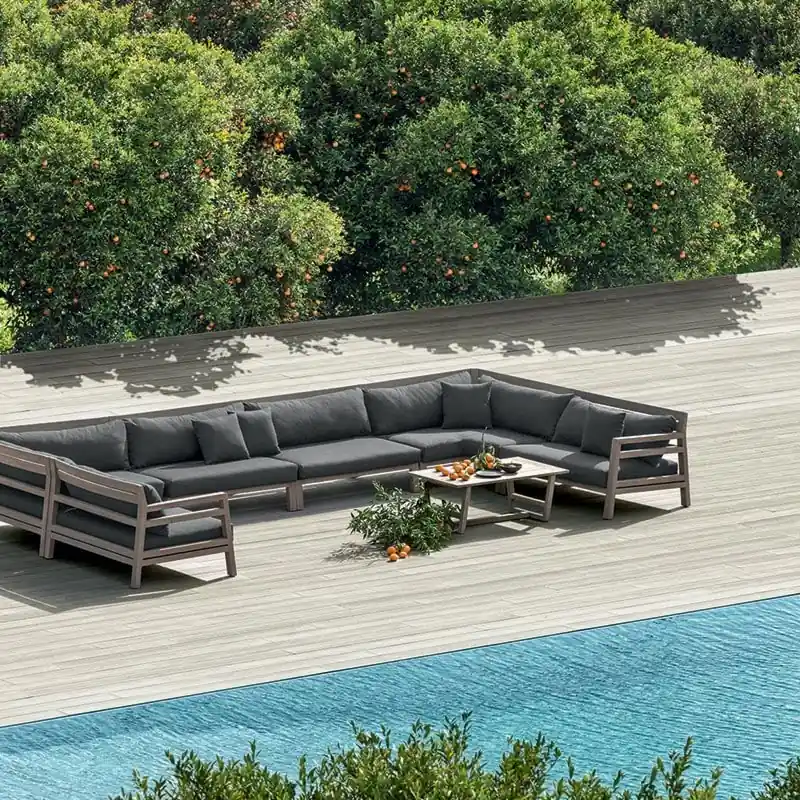 Ethimo Costes corner sofa with dark cushions on a wooden deck above a turquoise pool, with the sea beyond