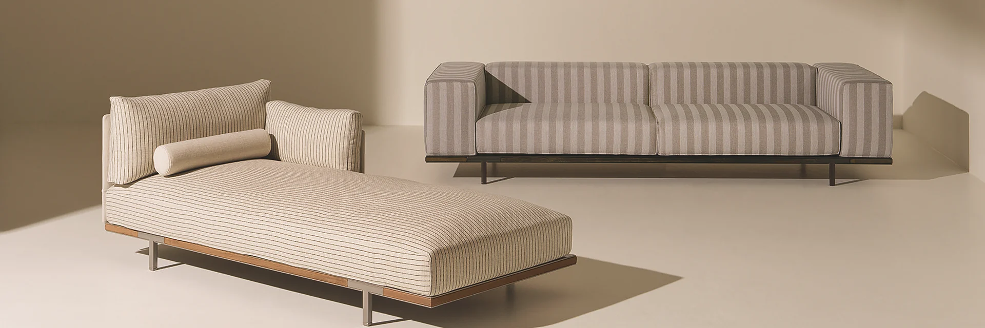 Ethimo Costiera chaise longue and a striped Costiera sofa in a sand-coloured setting with soft sunlight
