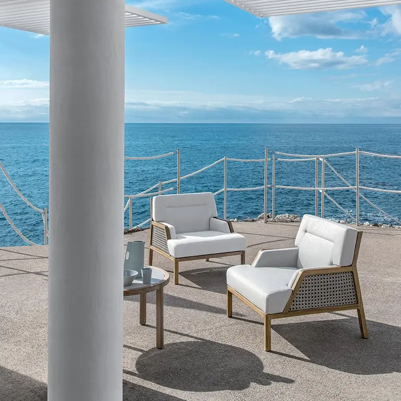 Ethimo Grand Life bergere armchairs with white cushions on a terrace with a white column, the open sea behind