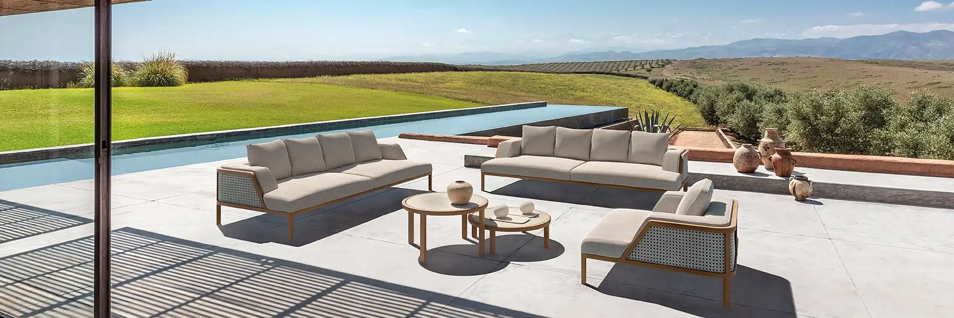 Ethimo Grand Life sofas and coffee tables on the terrace of a modern house, with a pool and open fields beyond