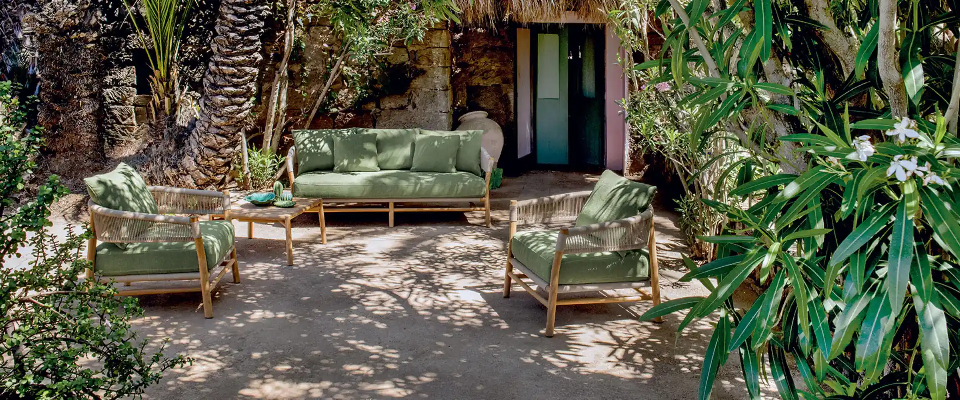 Ethimo Kilt teak sofa and lounge armchairs with green cushions in a shady garden of palms and lush plants