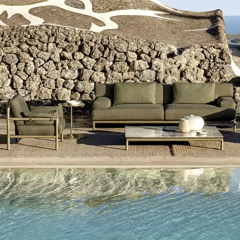 Ethimo Lodge sofa, armchairs and coffee table with green cushions at the edge of a pool, below a lava-stone wall
