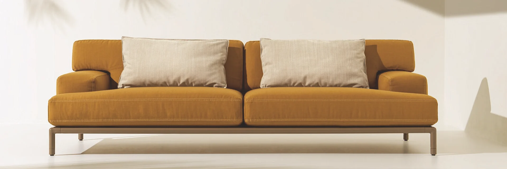 Ethimo Lodge two-seater sofa in ochre fabric with cream cushions, in a sunlit cream setting