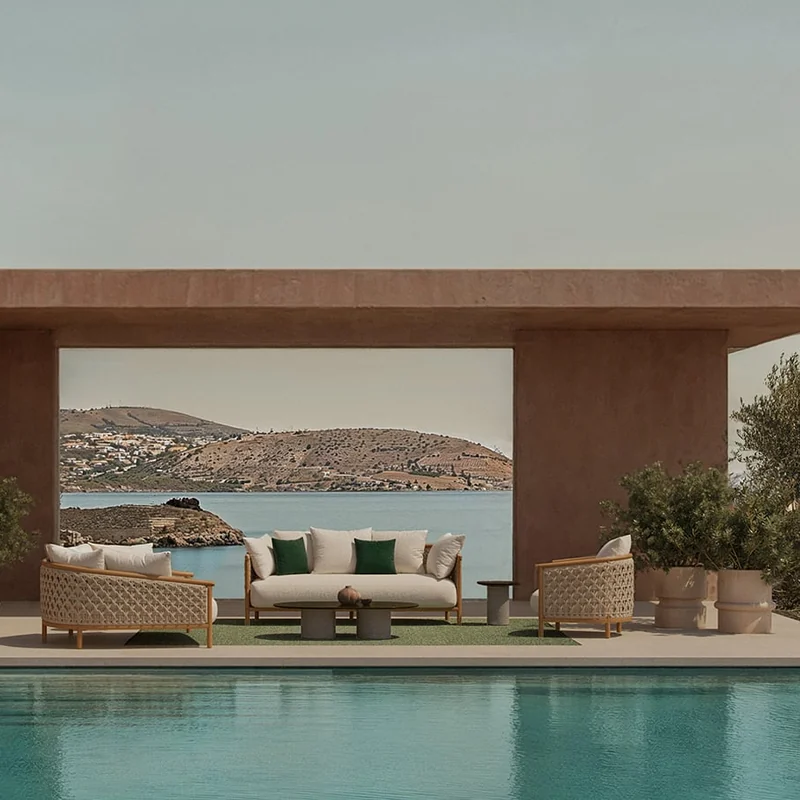 Ethimo Patio sofa and armchairs under a terracotta-colored pavilion beside a turquoise pool, with a bay in the distance