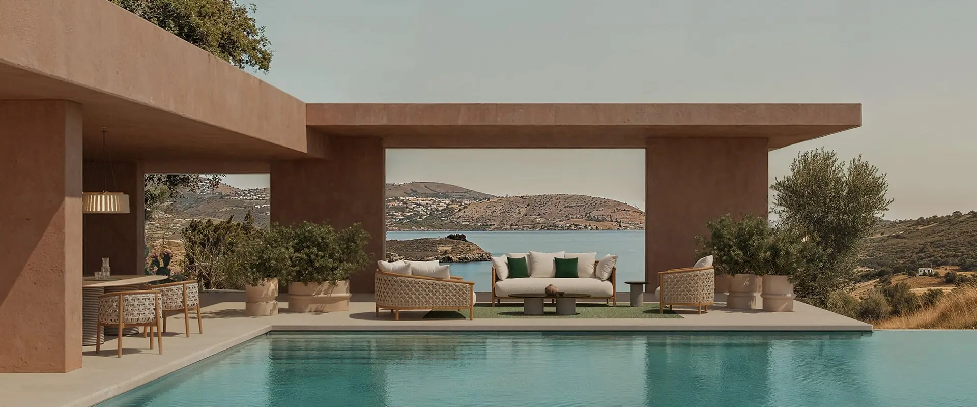 Ethimo Patio sofa and armchairs under a terracotta-colored pavilion beside a turquoise pool, with a bay in the distance