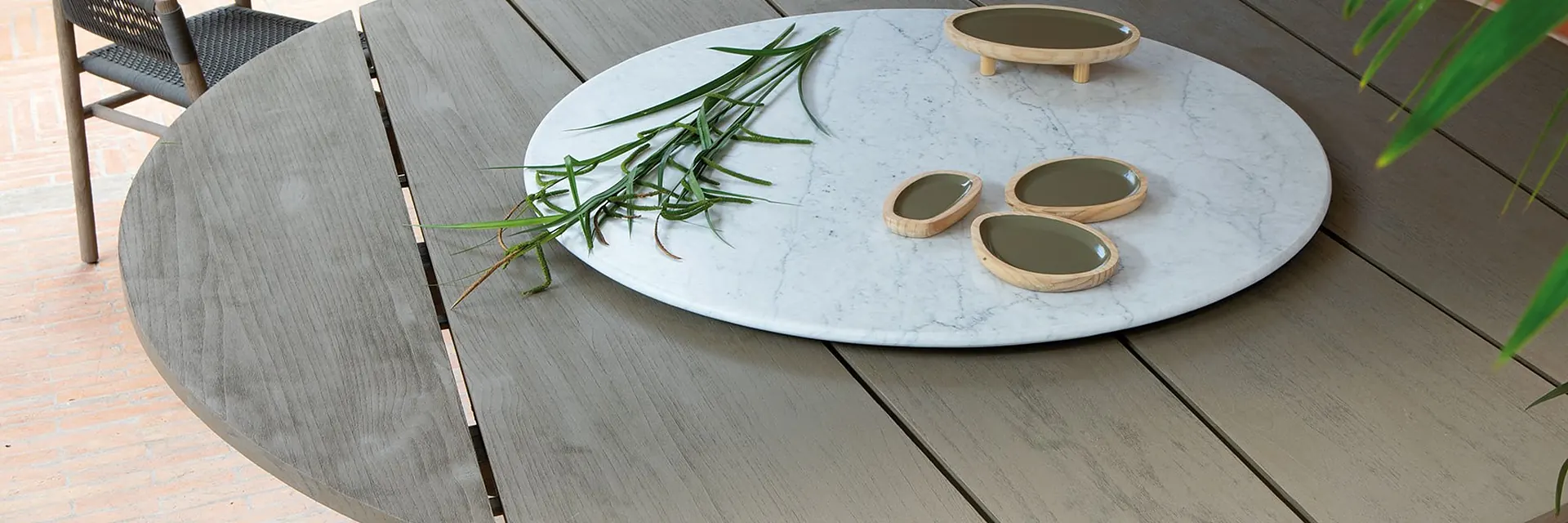 Close view of an Ethimo Rafael round teak table with a white lazy Susan, with a rope chair beside it