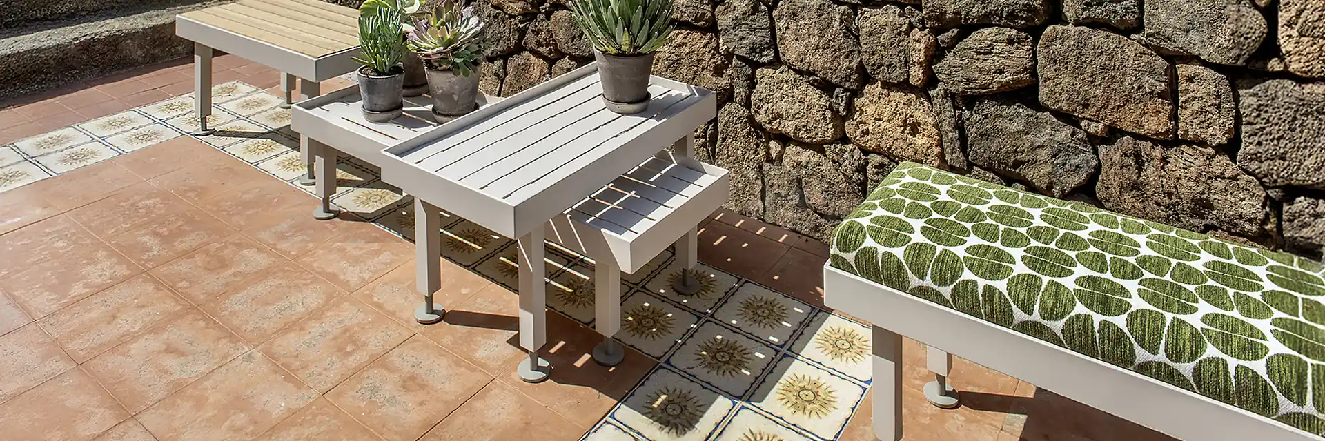Ethimo Seeds benches and low table with potted succulents on a tiled terrace beside a dry-stone wall