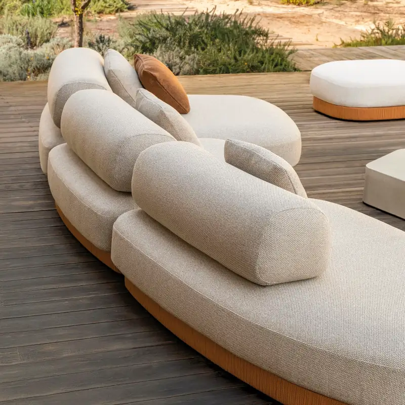 Expormim Brae curved modular sofa in cream fabric with a round ottoman on a wooden deck, a dry garden behind