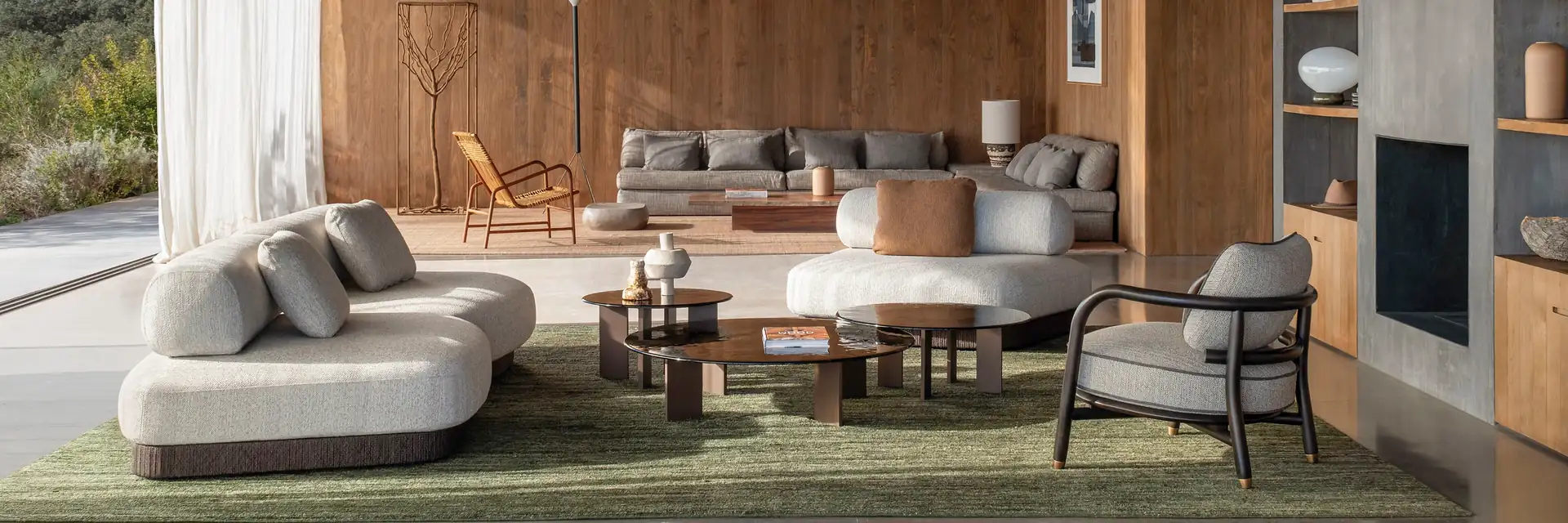 Expormim Brae curved modular sofa and an armchair on a green rug in a timber-lined living room open to the garden