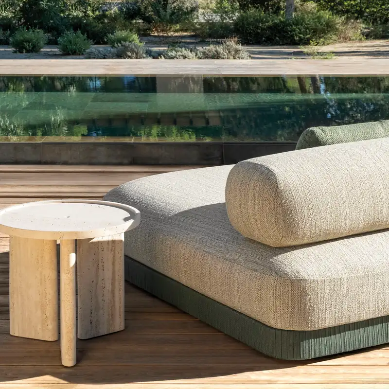 Expormim Brae sofa with a rounded bolster back in cream fabric and a pale stone side table, beside a long pool