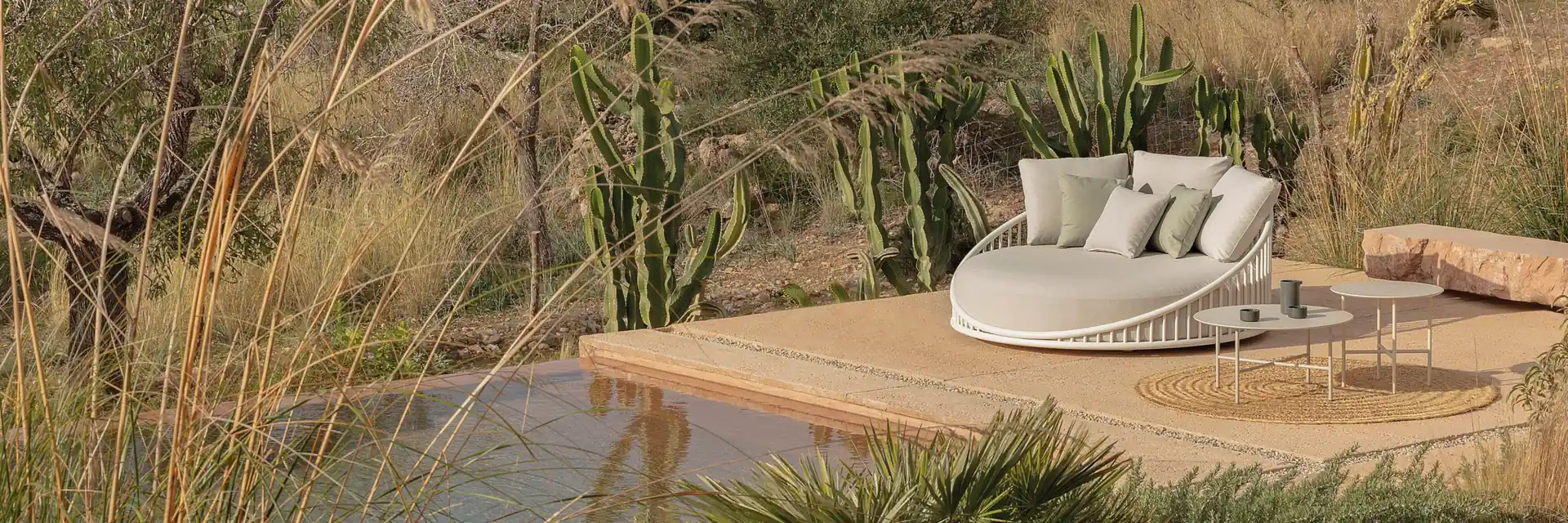 Expormim Cask round daybed with cushions on a deck over a pond, among tall grasses and cacti