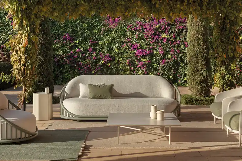 Expormim Cask outdoor sofa and armchairs under a reed-roofed pergola, in front of a wall of bougainvillea