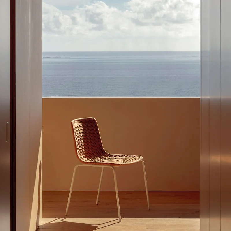 Expormim Lapala hand-woven chair on a terracotta terrace, framed by an opening onto the sea and a cloudy sky