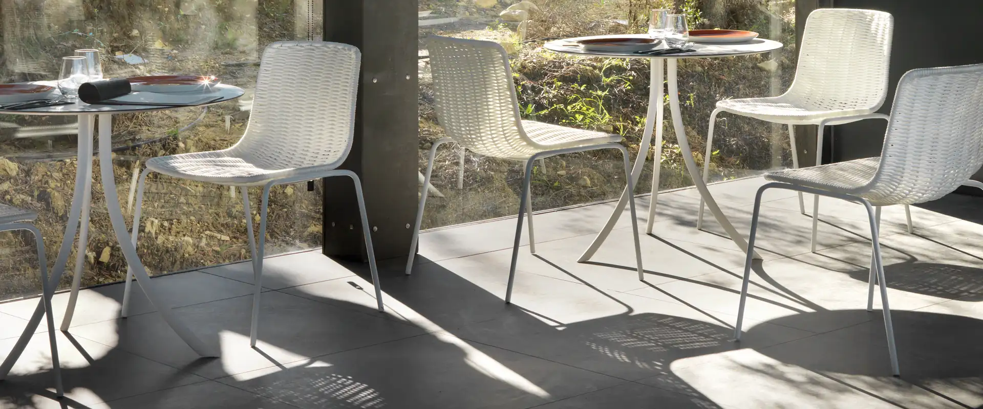 Expormim Lapala chairs in white around small round tables under a pergola, with a sunlit garden behind