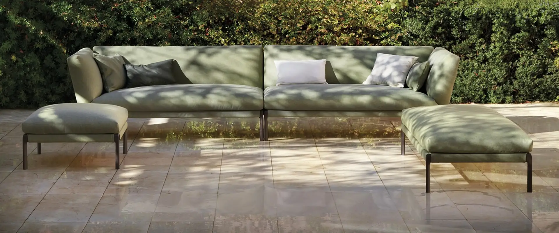 Expormim Livit modular outdoor sofa in sage green in a paved courtyard, in front of a wall of climbing plants