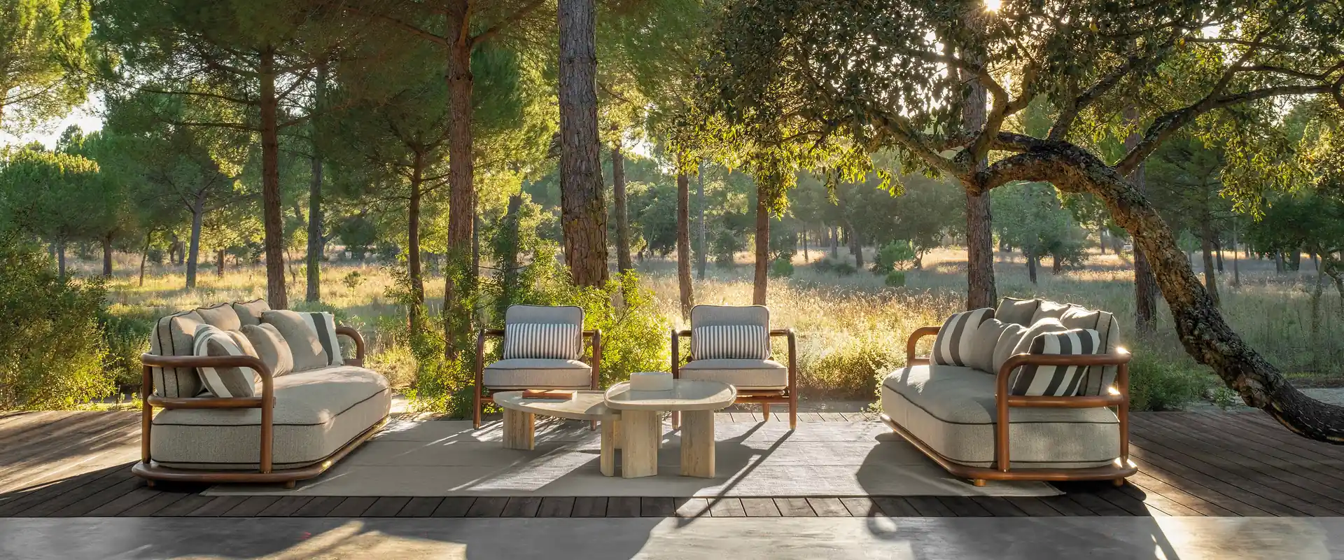 Expormim Meridies sofas and armchairs with striped cushions on a deck under a timber roof, among pine trees at sunset