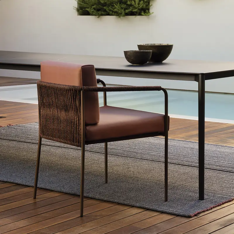 Expormim Nido dining chair with a woven back and a tan seat at a dark table on a deck by a pool