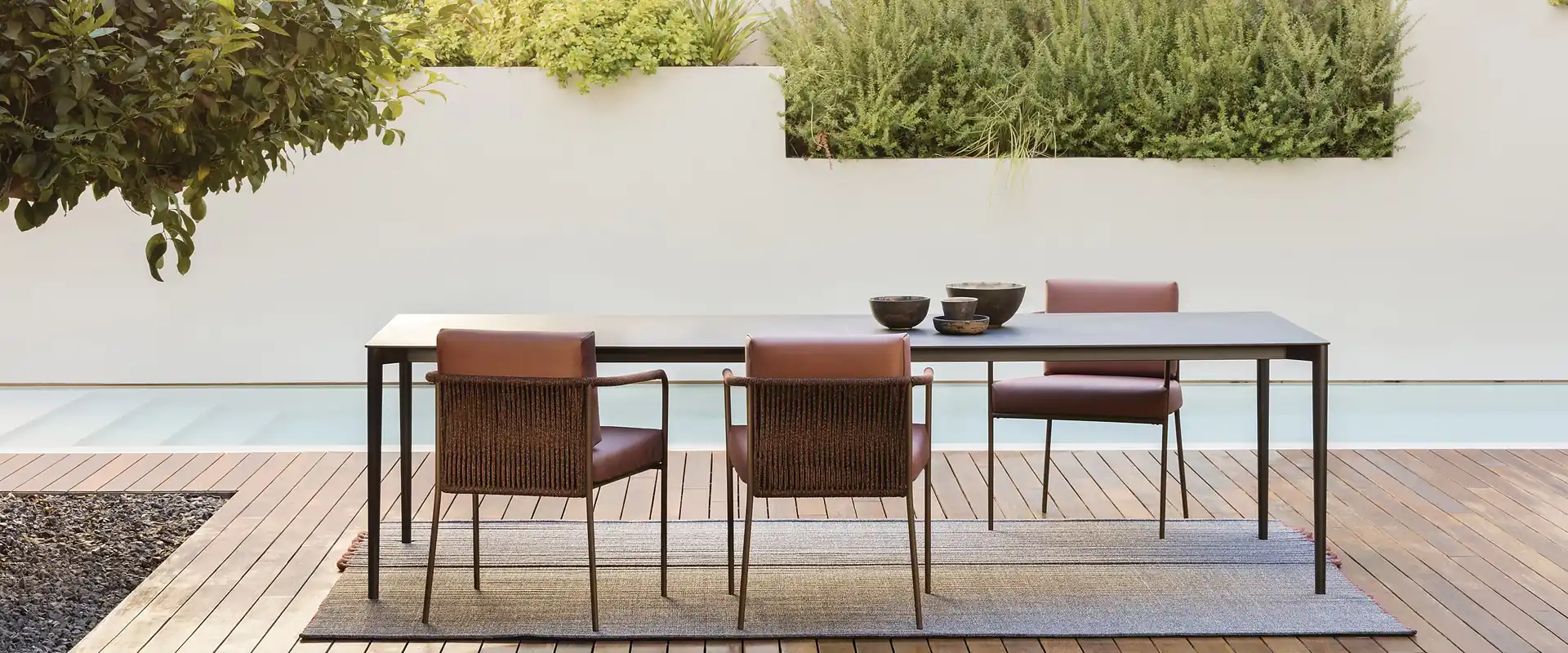 Expormim Nido dining chairs with terracotta upholstery around a long table on a wooden deck, white walls and planters behind
