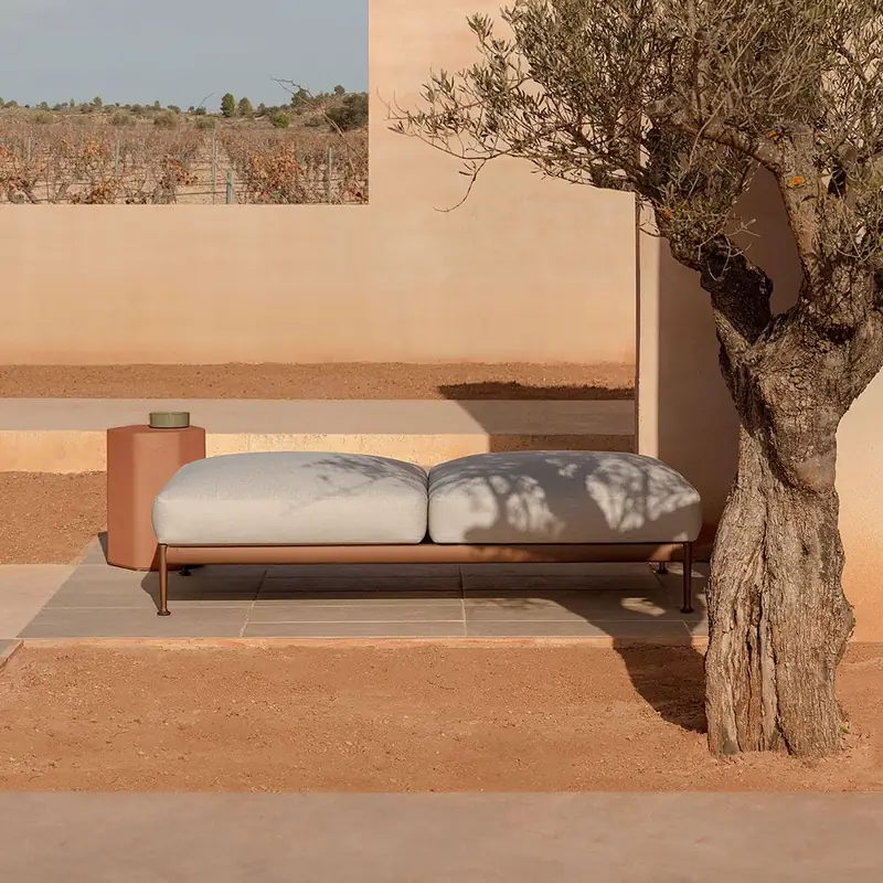 Expormim Obi daybed with pale cushions on a terracotta terrace beside an old olive tree and earthen walls