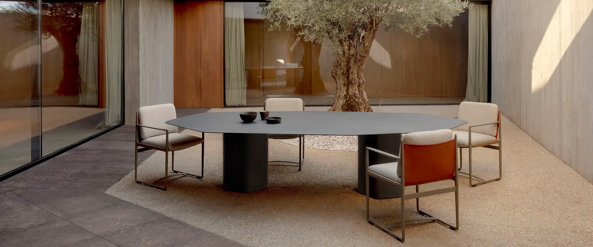 Expormim Obi dining armchairs around an oval table in a concrete courtyard with an old olive tree