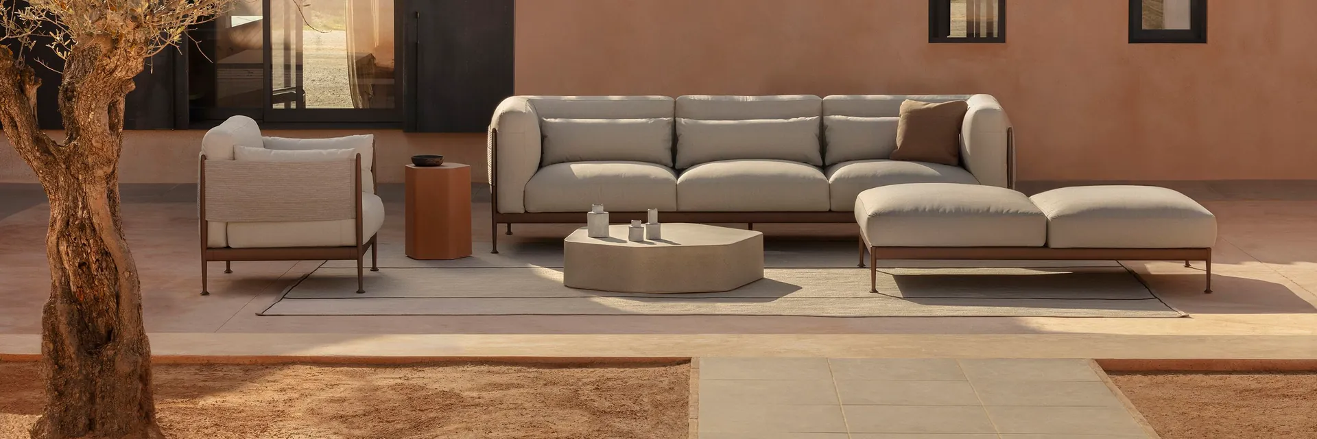 Expormim Obi modular sofa and armchair in a courtyard in front of a terracotta-coloured house with a tiled roof, beside an old olive tree