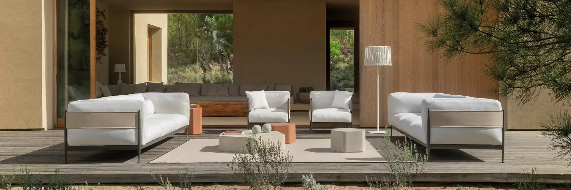 Expormim Obi sofas and armchairs on a timber deck in front of an ochre house with a large opening onto the garden