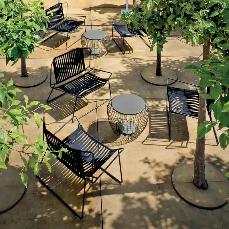 Expormim Out-Line armchairs in black rope with round tables on a gravel patio among young trees, seen from above