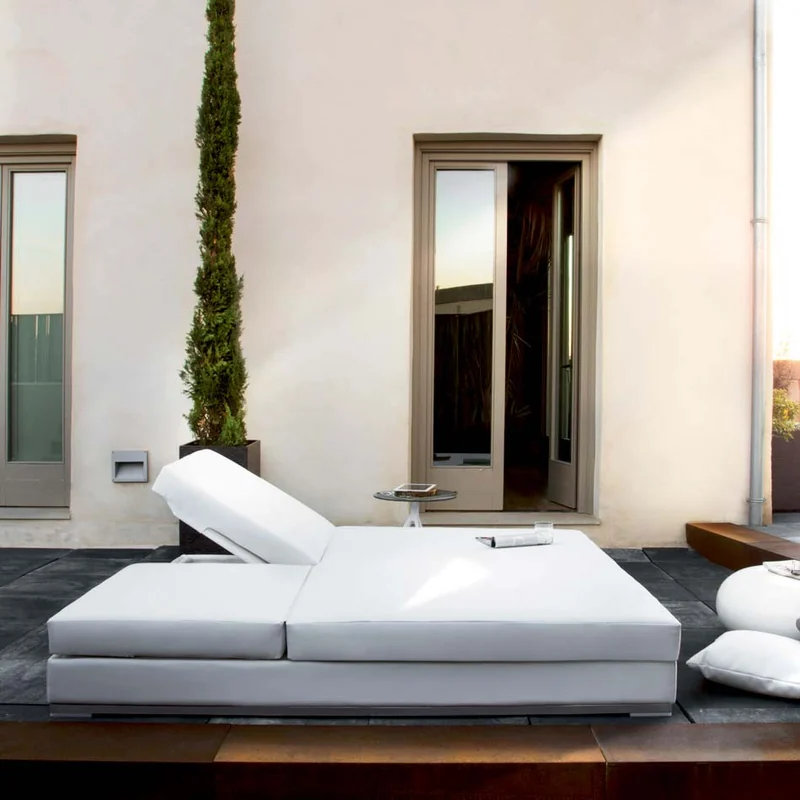 Expormim Slim double chaise longue with white cushions on a dark terrace in front of a white house with a cypress
