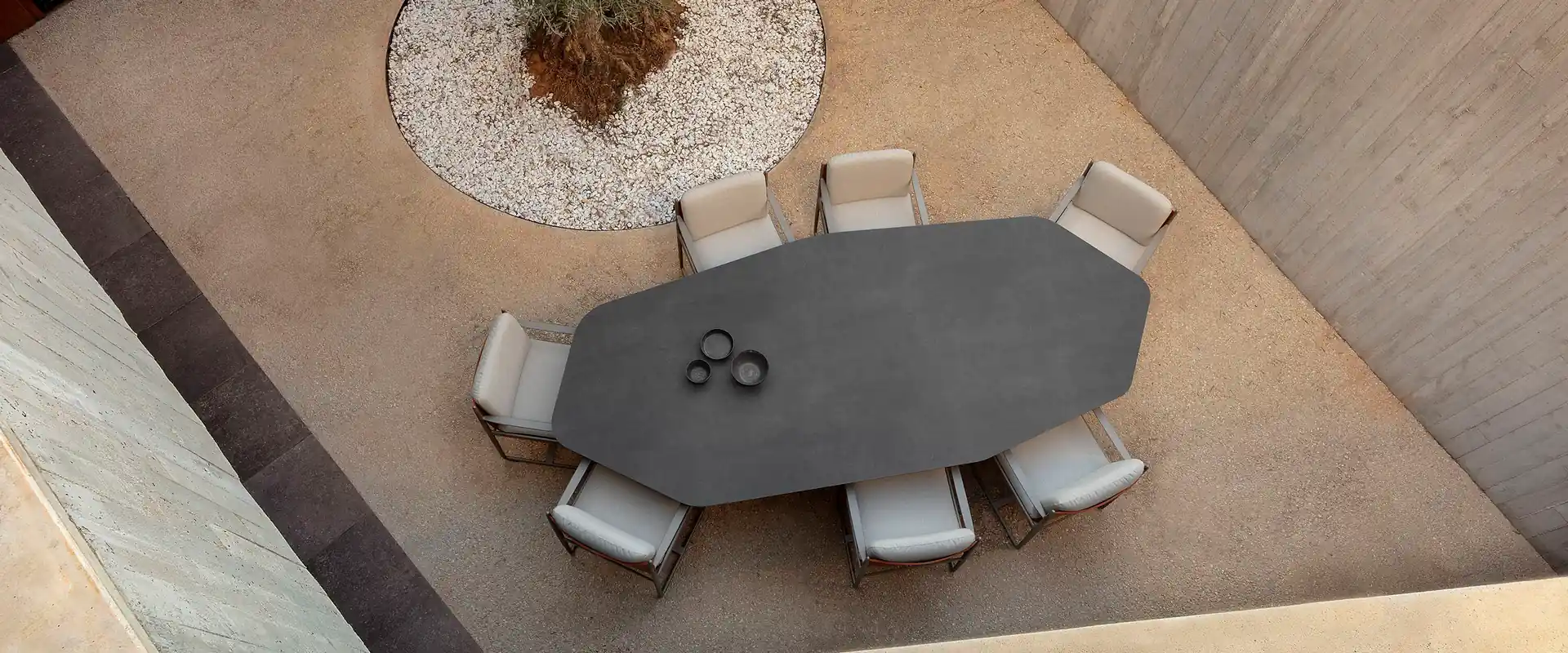 Expormim Talo octagonal dining table with pale armchairs in a stone courtyard with a tree, seen from above