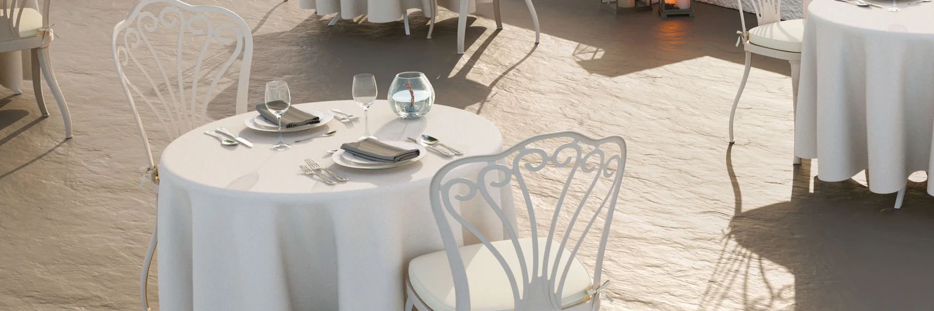 Fast Armonia white aluminum chairs at round tables with white tablecloths on a terrace over the sea at sunset