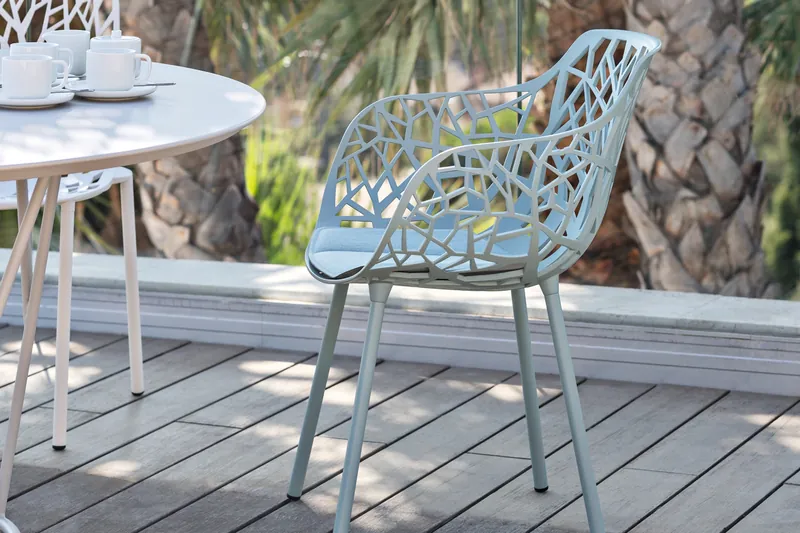 Pale blue Fast Forest aluminium armchair at a round white table on a decked terrace, in front of palm trunks