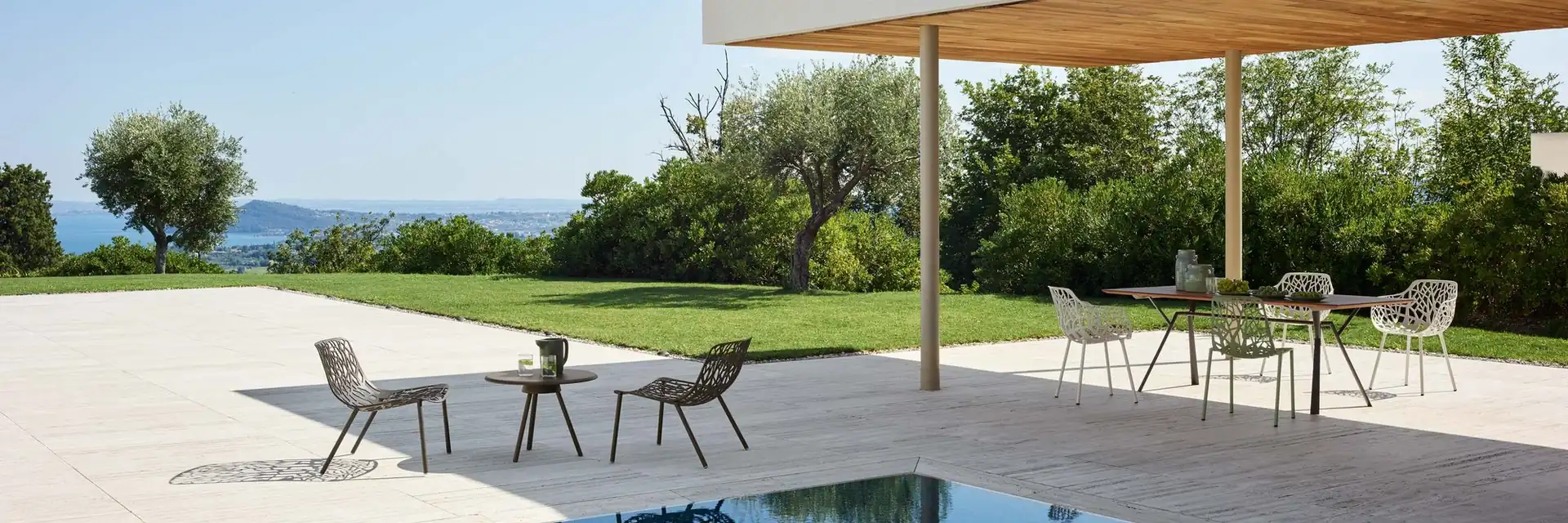 Fast Forest armchairs around a dining table under the canopy of a modern villa, with low Forest lounge chairs beside the pool
